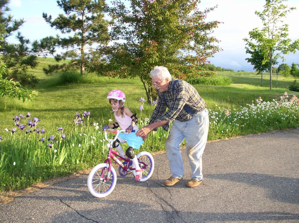 grandfather helping granddaughter learn to ride bicycle - child is wearing a bike helmet